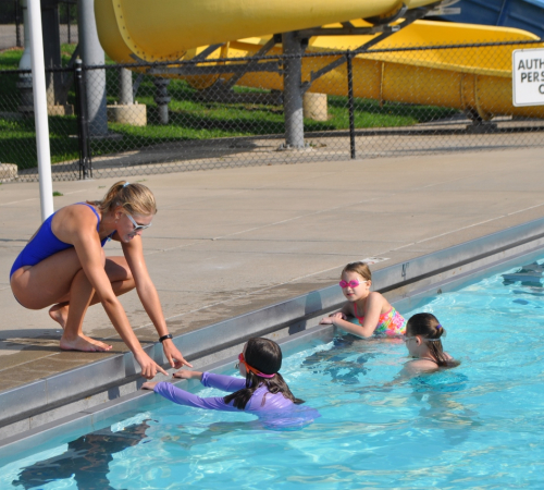 children in pool look at young woman bending into pool to teach