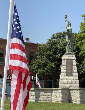 American flag placed in the ground at City Hall with miniature Statue of Liberty in the background