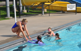 children in pool look at young woman bending into pool to teach