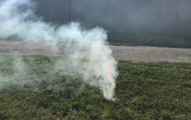 Photo of smoke coming out of a manhole in a green field outside