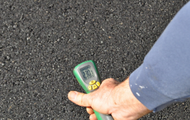 Digital readout of thermometer on recently paved asphalt shows 230.7 degrees Fahrenheit