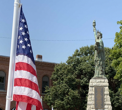 American flag placed in the ground at City Hall with miniature Statue of Liberty in the background