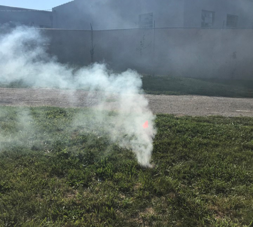 Photo of smoke coming out of a manhole in a green field outside