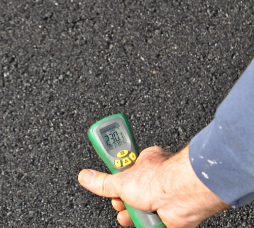 Digital readout of thermometer on recently paved asphalt shows 230.7 degrees Fahrenheit