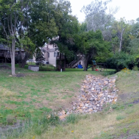 Photo of rip rap along new drainage ditch surrounded by green grass, trees and behind homes
