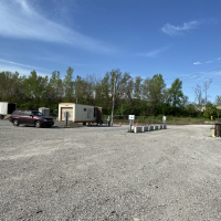 Entrance to the Leavenworth Brush Site, several piles of brush and yard waste on a gravel lot with a trailer office and vehicles