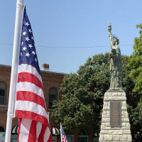 American flag placed in the ground at City Hall with miniature Statue of Liberty in the background