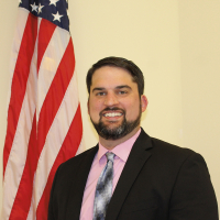 Image of man standing next to an American flag wearing a long necktie and black blazer