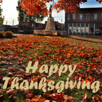Tree with orange leaves, some on the ground, around mini Statue of Liberty, Leavenworth city logo text reads Happy Thanksgiving