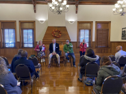 Multiple presenters talk to seated crowd