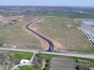 Overhead photo shows empty field adjacent to several large businesses with newly constructed road