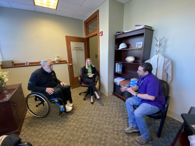 Man in wheelchair visits city staff inside city offices to talk about accessibility issues.